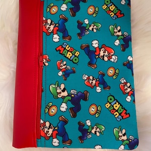May include: A red zippered pouch with a turquoise background featuring a repeating pattern of Super Mario characters. The text "Super Mario" is printed on the pouch.