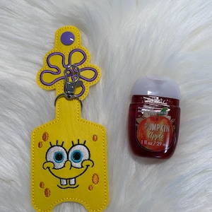 May include: A yellow Spongebob Squarepants keychain with a silver clasp next to a red hand sanitizer bottle with a white cap. The hand sanitizer bottle has a label that says "Pumpkin Apple".