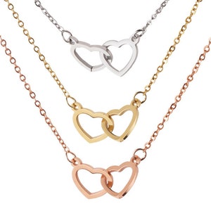 May include: Three layered necklaces with interlocking heart pendants. The top necklace is silver, the middle necklace is gold, and the bottom necklace is rose gold.