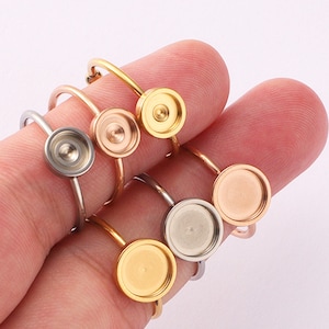 May include: Five adjustable rings with round, bezel-set, silver, gold, and rose gold settings. The rings are made of metal and are designed to hold a cabochon.