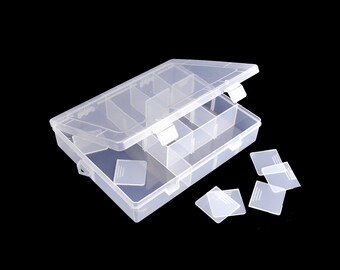 Può includere: Una scatola organizzatrice rettangolare in plastica trasparente dotata di coperchio incernierato con chiusura a scatto. L'interno è suddiviso in più scomparti da divisori rimovibili, con alcuni divisori quadrati piatti in plastica posizionati accanto.