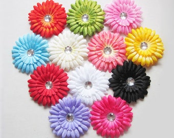 May include: A collection of twelve artificial daisy-like flowers arranged in a cluster. Each flower features layered petals in vibrant colors including red, lime green, pink, light blue, white, yellow, black, purple, and magenta, with a clear rhinestone.