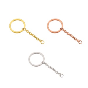 May include: Three metal keychains, each featuring a circular split ring attached to a short link chain. The set includes one gold-toned, one rose gold-toned, and one silver-toned keychain, all displayed against a plain white background.