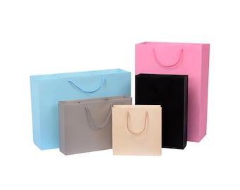 May include: Five paper gift bags in different sizes and colors. The bags are light blue, gray, beige, black, and pink. The bags have rope handles.