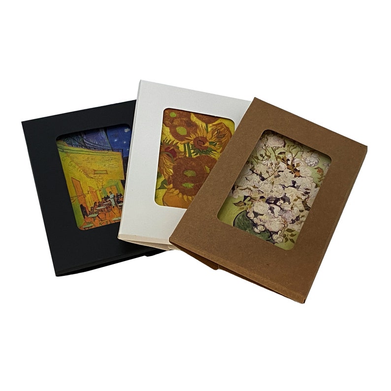 May include: Three different card boxes with different designs. The first box is black with a white image of a cafe interior. The second box is white with a yellow image of sunflowers. The third box is brown with a white image of white flowers.