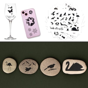 May include: A clear wine glass with black butterfly decals and the text Butterfly Love, a light pink smartphone case with black star and geometric designs, a stack of white sheets with black bird silhouettes, and four smooth stones with black bird prints.