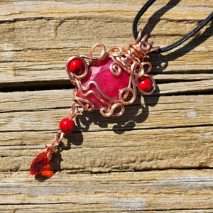 May include: A red gemstone pendant wrapped in copper wire with red beads and a black cord.