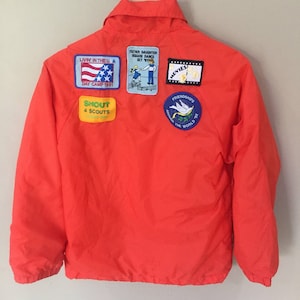 May include: Orange jacket with multiple patches, including "Living in the U.S.A. Day Camp 1991", "Father Daughter Square Dance Oct '91", "Movies", "Shout 4 Scouts", and "Friendships Around the World 92".