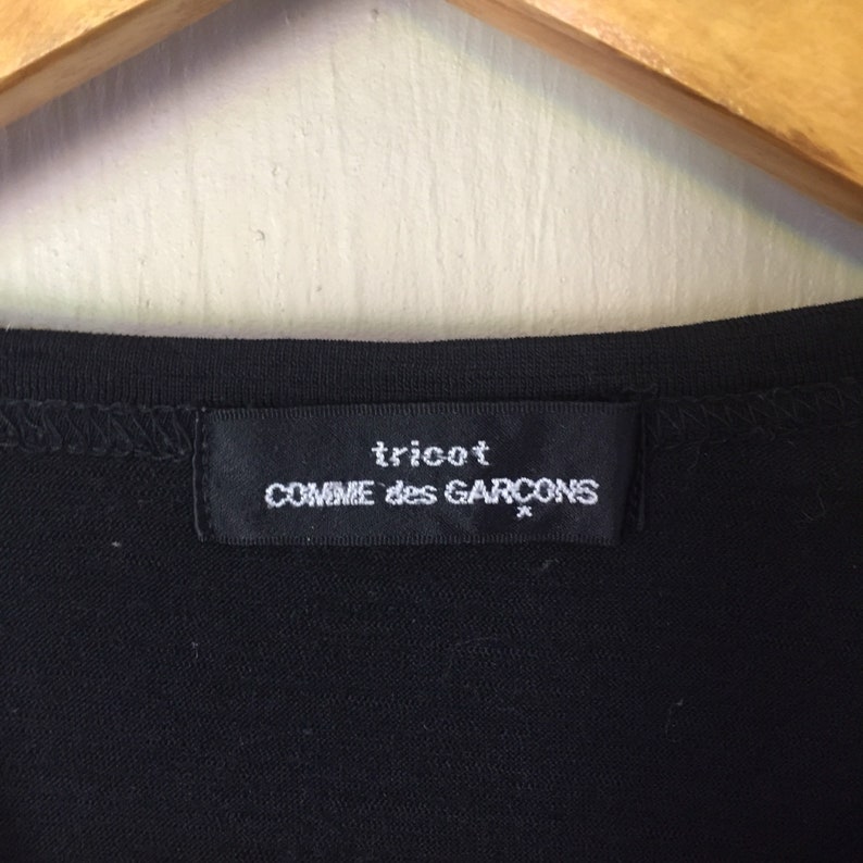 May include: Black tricot Comme des Gar&ccedil;ons label tag on a black garment.
