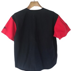 Puede incluir: Una camiseta de b&eacute;isbol negra y roja con un logotipo blanco en la manga izquierda.