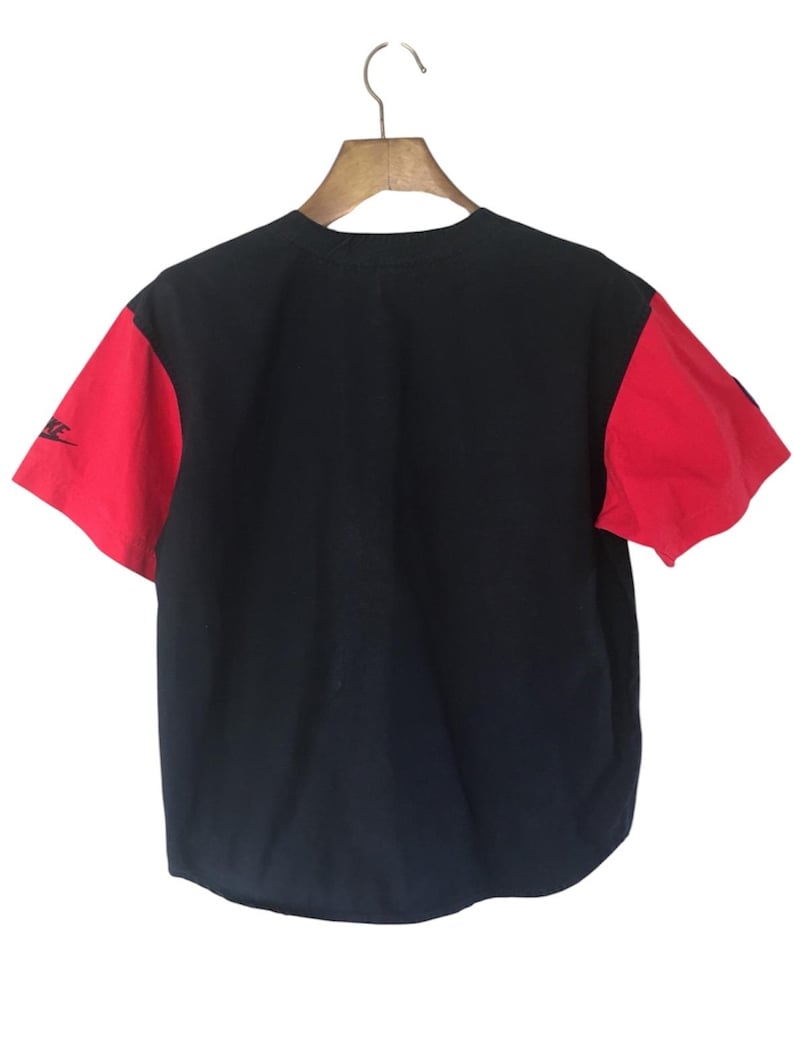 Puede incluir: Una camiseta de b&eacute;isbol negra y roja con un logotipo blanco en la manga izquierda.