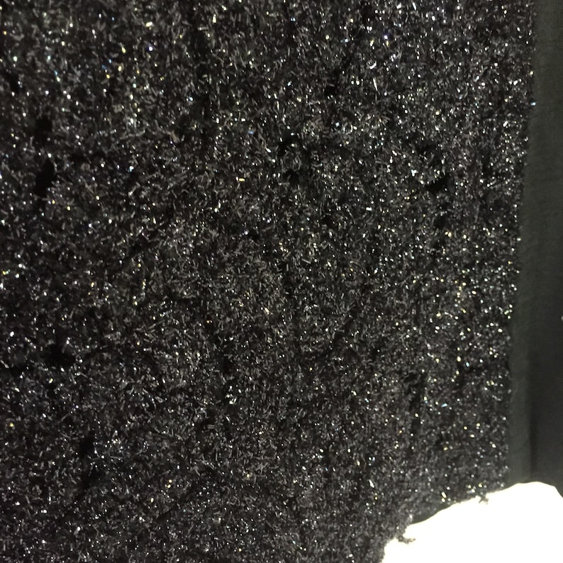 May include: Black textured fabric with a sparkly, glittery finish. The fabric has a rough, uneven surface.
