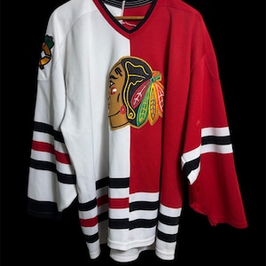 May include: A vintage hockey jersey, divided into white and red sections. The jersey displays the team emblem on the chest and shoulder, with black and red stripes on the sleeves and hem. The V-neck collar is black.