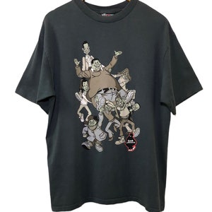 May include: A dark green t-shirt featuring a cartoon graphic of a group of people. The graphic depicts a large man with a group of smaller people surrounding him. The text "Fat Albert" is visible on the bottom right of the graphic.
