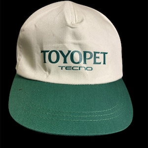 May include: A baseball cap featuring a cream-coloured crown and a green peak. The text "TOYOPET" is printed in green across the front, with "TECNO" underneath. The cap is made of a sturdy fabric.