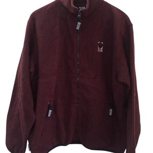 May include: A maroon fleece zip-up jacket with a black zipper and black trim. The jacket has a small logo on the chest that says "Reconsider"