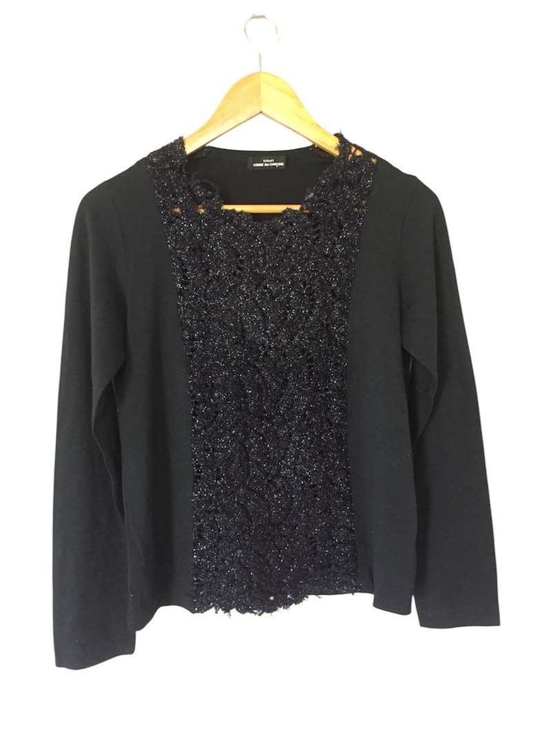 May include: Black long-sleeve sweater with a black lace overlay on the front. The sweater has a round neckline and long sleeves.