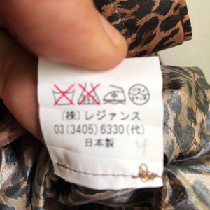 May include: A white care label with black and red symbols and text. The text reads: "(株) レジァンス 03 (3405) 6330 (代) 日本製 4".