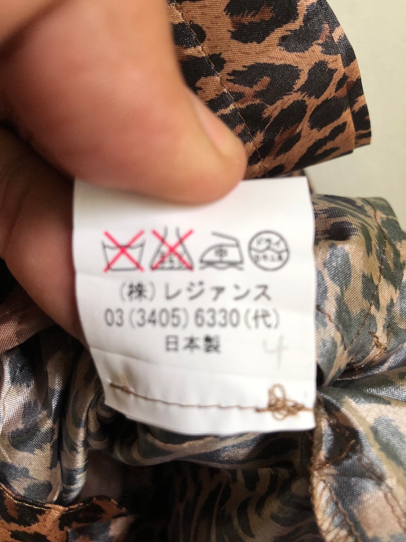 May include: A white care label with black and red symbols and text. The text reads: "(株) レジァンス 03 (3405) 6330 (代) 日本製 4".