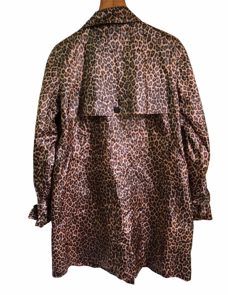 May include: A long-sleeved leopard print raincoat with a button closure and a belt at the back.