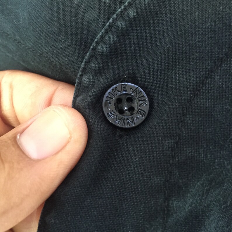 Puede incluir: Un bot&oacute;n negro con la palabra "NIKE" en relieve en letras blancas alrededor del bot&oacute;n.