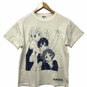 Pode incluir: Uma camiseta branca com uma ilustração azul e branca de três personagens de anime. Os personagens são uma menina com cabelo comprido, um menino com cabelo curto e uma menina com cabelo curto. O texto "ご注文はうさぎですか?" está impresso na parte inferior da camiseta.