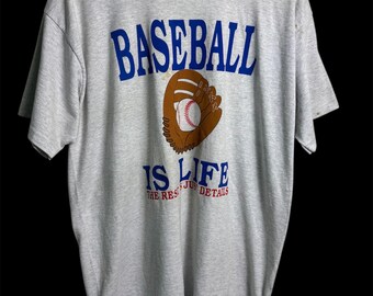Könnte beinhalten: Graues Baseball-T-Shirt mit dem Schriftzug "BASEBALL IS LIFE" in Blau und Weiß. Eine Baseballhandschuh-Grafik mit einem Baseball ist unter dem Text zentriert. Das Shirt ist aus weichem Material.