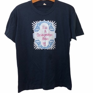 以下が含まれることがあります： 紺色のTシャツに、白で「I'm a Computer Star」というピンクと青の文字のグラフィックがプリントされています。グラフィックは青と白の星形のバーストで囲まれています。