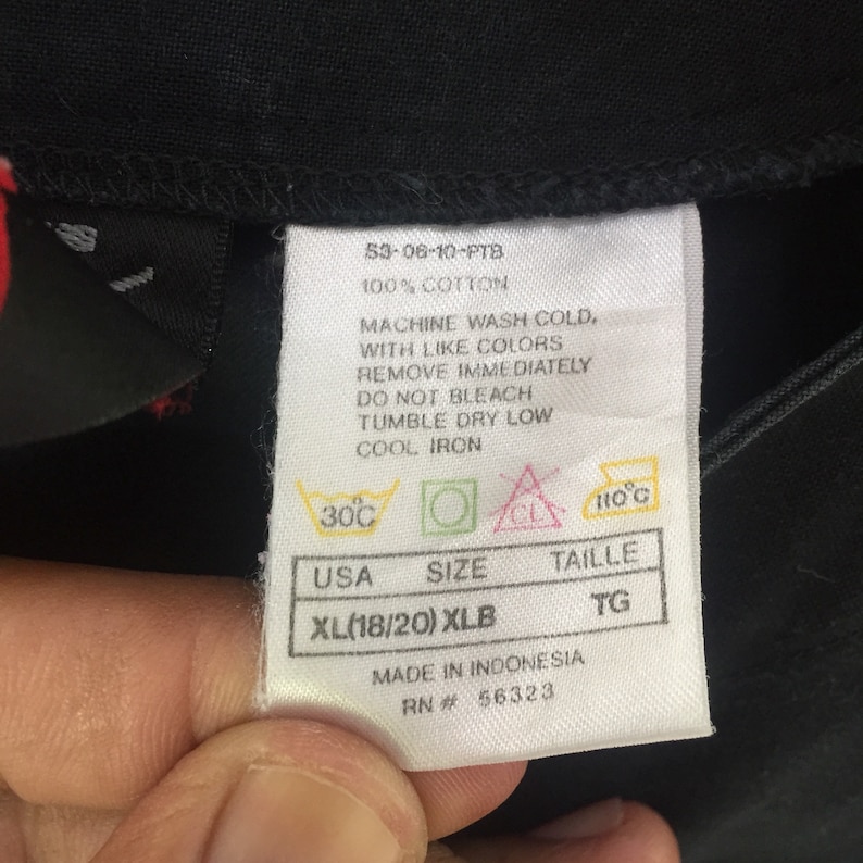 Puede incluir: Una etiqueta blanca con texto negro y s&iacute;mbolos. La etiqueta tiene instrucciones de cuidado para una prenda, incluyendo lavar a m&aacute;quina con agua fr&iacute;a, secar en secadora a baja temperatura y planchar a baja temperatura. La etiqueta tambi&eacute;n incluye la talla XL (18/20) XLB, USA, y el n&uacute;mero RN 56323. La etiqueta est&aacute; hecha en Indonesia.