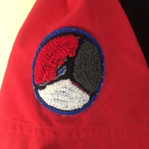 Puede incluir: Parche bordado circular rojo, blanco y azul con un dise&ntilde;o de p&aacute;jaro estilizado. El parche tiene un borde azul.