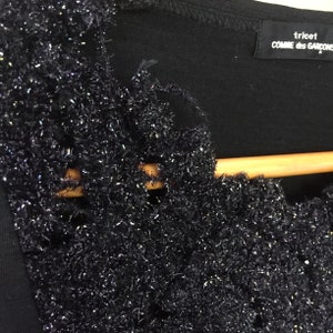 May include: Black shirt with a sparkly, textured trim around the neckline. The shirt has a label that reads "tricot COMME des GARCONS".