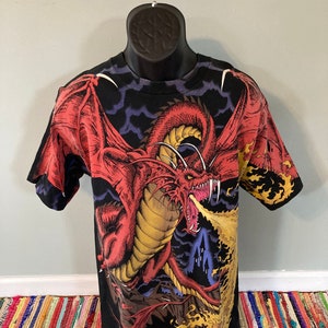 May include: Black t-shirt with a red dragon breathing fire in front of a dark castle. The dragon has yellow accents and is set against a dark blue and purple sky.