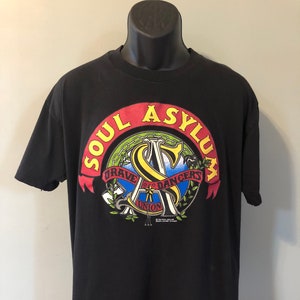 May include: Black t-shirt with a graphic of a circle with the words "Soul Asylum" in red and yellow. Inside the circle is a stylized "S" with the words "Brave New Dancers" and "Union" around it.