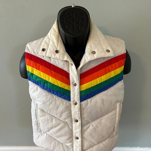 May include: A white puffer vest with a rainbow stripe design. The vest has a snap closure and a stand-up collar.