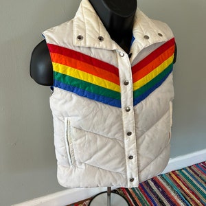 May include: White puffer vest with a rainbow stripe design. The vest has a snap closure and a stand-up collar.