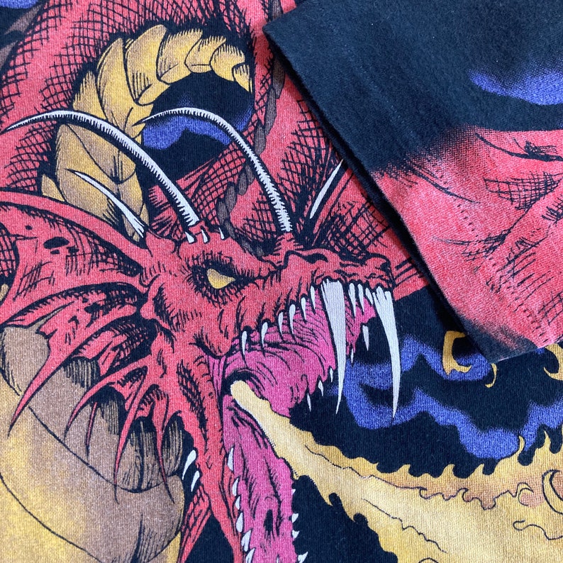 May include: A black t-shirt with a red, yellow, and blue dragon graphic. The dragon is depicted with a fierce expression and sharp teeth.