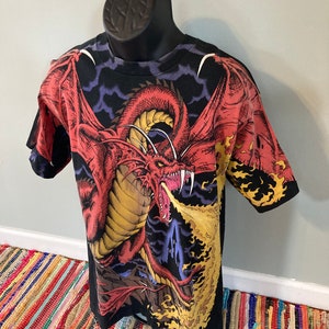 May include: Black t-shirt with a red dragon breathing fire graphic print. The dragon is set against a dark blue and purple background with clouds.