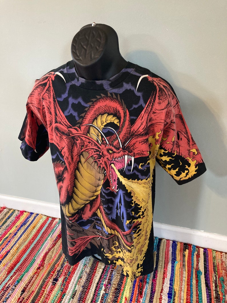 May include: Black t-shirt with a red dragon breathing fire graphic print. The dragon is set against a dark blue and purple background with clouds.