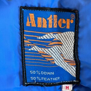 May include: A blue and orange patch with the word "Antler" in orange lettering and the text "50% Down 50% Feather" in white lettering. The patch has a white and orange design with a black border.