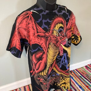 May include: Black t-shirt with a red dragon breathing fire, set against a dark blue and purple cloudy sky.