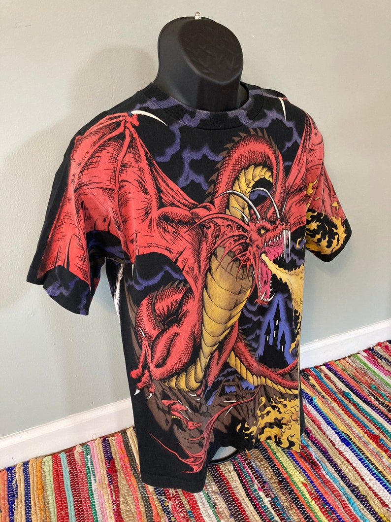 May include: Black t-shirt with a red dragon breathing fire, set against a dark blue and purple cloudy sky.