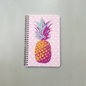 May include: A pink spiral notebook with a white polka dot pattern and a graphic of a yellow pineapple with a pink and blue design.