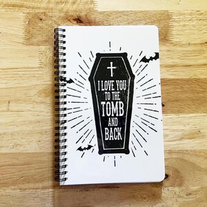May include: A black and white spiral notebook with a coffin design and the text "I love you to the tomb and back".
