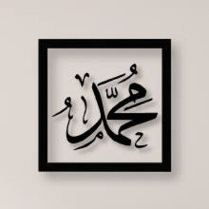 May include: Black framed wall art featuring Arabic calligraphy in a white font. The calligraphy reads "Muhammad" in Arabic.
