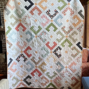 May include: A large, handmade quilt with a white background and a repeating pattern of colorful, interlocking C-shapes. The C-shapes are in shades of peach, green, blue, and black, with floral and patterned fabric accents. The quilt is displayed on a wooden surface.