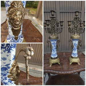 May include: A pair of tall candelabras featuring blue and white floral porcelain bodies with ornate brass bases, handles, and five-arm candle holders. Each piece is decorated with a prominent brass lion head relief and intricate metal scrollwork.