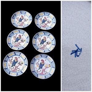May include: Six ceramic plates with a blue and white design. Each plate features a colourful parrot perched on a branch with flowers. The plates have a blue patterned border and are set against a black background.