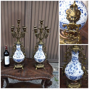 Può includere: Una coppia di candelabri a cinque bracci con basi in porcellana blu e bianca a motivi floreali. I candelabri presentano decorazioni in ottone, inclusi dettagli a testa di leone e maniglie ad anello. Una bottiglia di vino funge da scala.