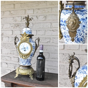 Könnte beinhalten: Eine antike blau-weiße Porzellan-Uhr mit Messingakzenten. Die Uhr hat ein rundes Zifferblatt mit römischen Ziffern und floralen Mustern. Eine Flasche Rotwein steht daneben.