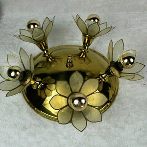May include: A vintage brass ceiling light fixture with five flower-shaped shades. Each shade has a clear, petal-like design and holds a round, gold-colored bulb. The fixture is mounted on a circular base with a central decorative element.